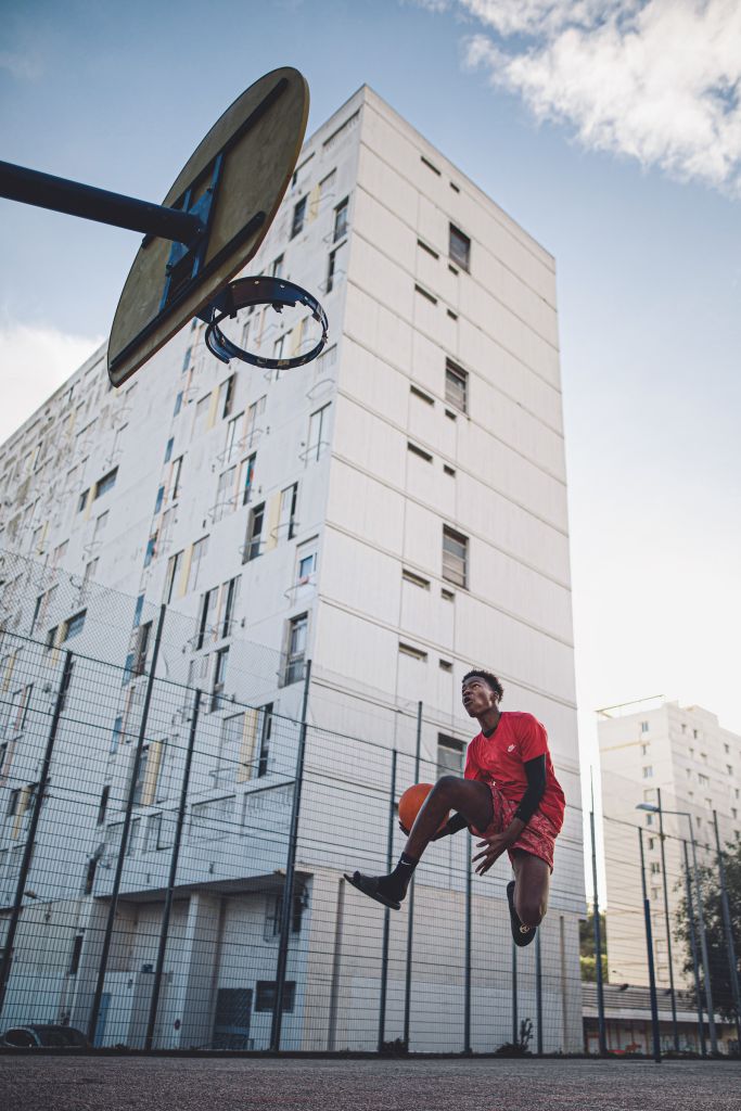 un collégien joue au basket au pied d'une barre HLM