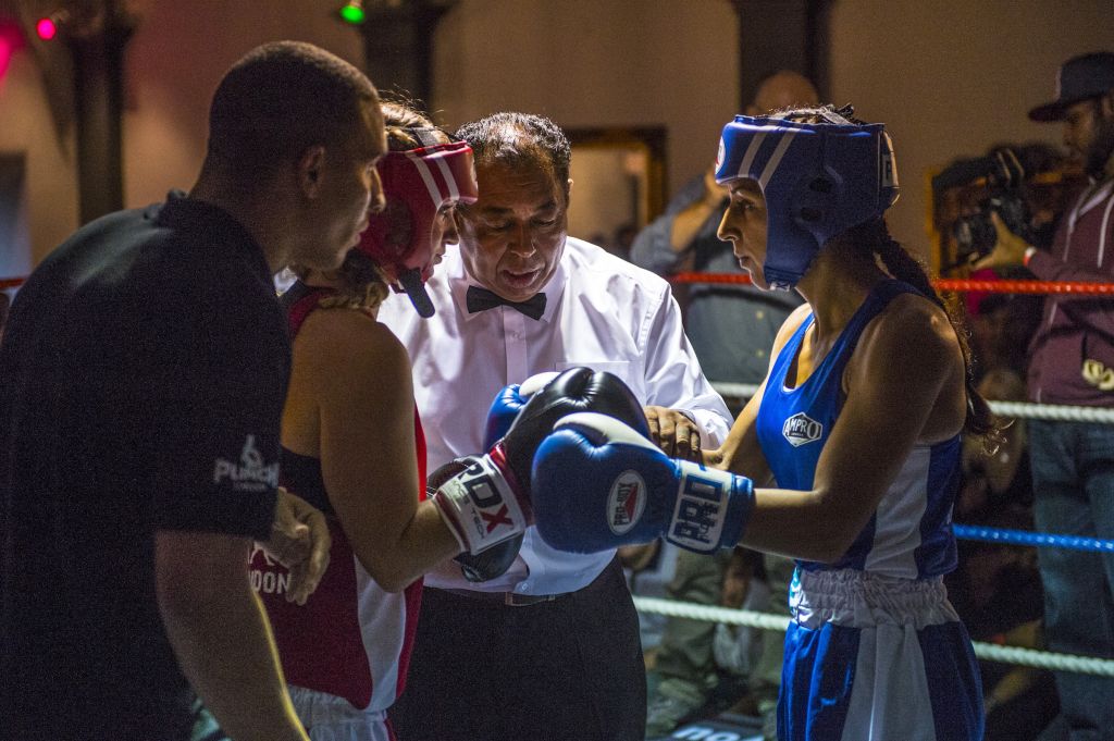 Emily Williams et son adversaire, Harvinder Jutte (en bleu), se défient du regard tandis que l’arbitre professionnel leur rappelle les règles de base. C’est la première fois que les deux femmes se rencontrent. L’adversaire d’Emily, 35 ans, travaille pour les services d’urgences londoniens. Elle est plus petite et plus légère que sa concurrente. C’est son troisième match : elle a gagné le premier, perdu le deuxième. « Certains combats ont des allures de bagarres de fin de soirées au pub. Ça n’a pas été le cas des six minutes qui ont suivi ce cliché. »