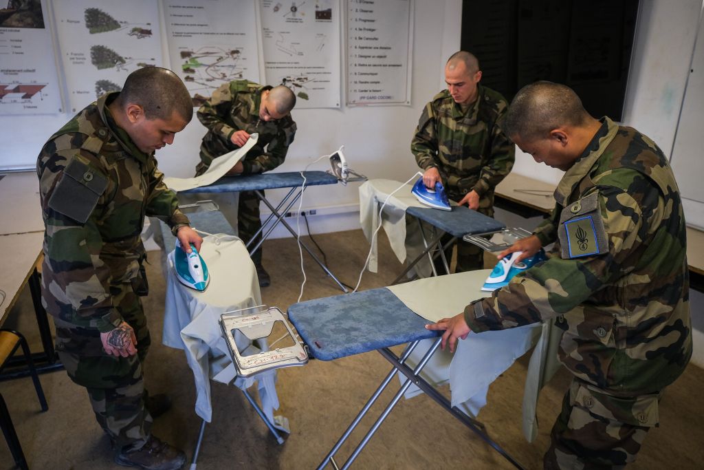 Dans une salle de cours, dont les murs sont tapissés d’affiches sur les manœuvres militaires, les aspirants repassent la tenue qu’ils porteront à leur remise de képi, la cérémonie marquant la fin de la première partie de la formation. La chemise doit être marquée de trois plis verticaux dans le dos, trois plis horizontaux au niveau des épaules, deux sur chaque manche, d’autres sur et sous les poches. Certains sont espacés de 53 millimètres, d’autres de 36. « C’est tellement compliqué et précis qu’ils doivent s’y prendre à plusieurs reprises. Lorsqu’ils ont réussi, ils mettent leur chemise sur un ceintre et n’y touchent plus jusqu’à la fin de leurs classes », s’amuse le photographe.