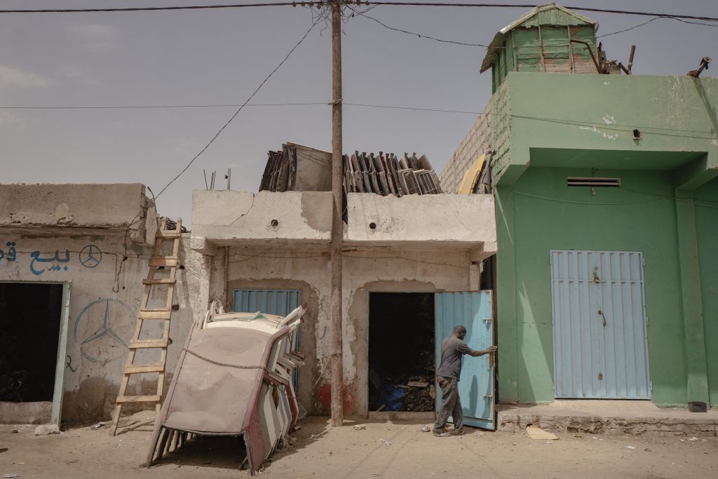 Dans le cœur historique de Nouakchott, le quartier de Ksar est le royaume des mécaniciens. La jeune ville s’est construite autour de ce paradis de la bricole. S’y alignent en rang désordonné une profusion de boutiques dans les tons pastel consacrées à la mécanique automobile de seconde main : casses auto, carrosseries, garages… Sur le toit de ce magasin de pièces détachées de Mercedes 190 sont entreposés des coffres du fameux modèle allemand. Devant, des toits découpés. « Cette voiture est très recherchée aussi, témoigne le photographe, parce que les pièces détachées sont partout et en grande quantité. »