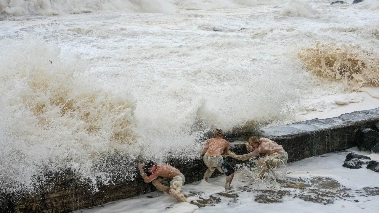trois hommes s’abritent derrière une digue où s’écrasent d’immenses vagues