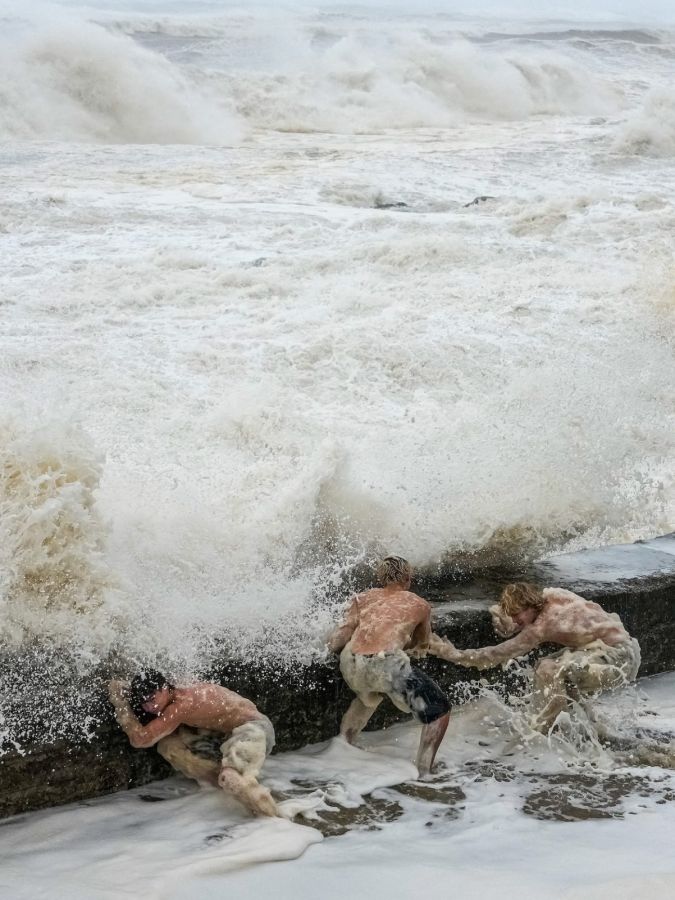 trois hommes s’abritent derrière une digue où s’écrasent d’immenses vagues