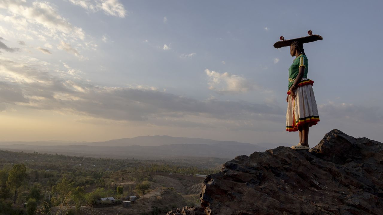 femme sur une colline, avec une planche de skate sur la tête