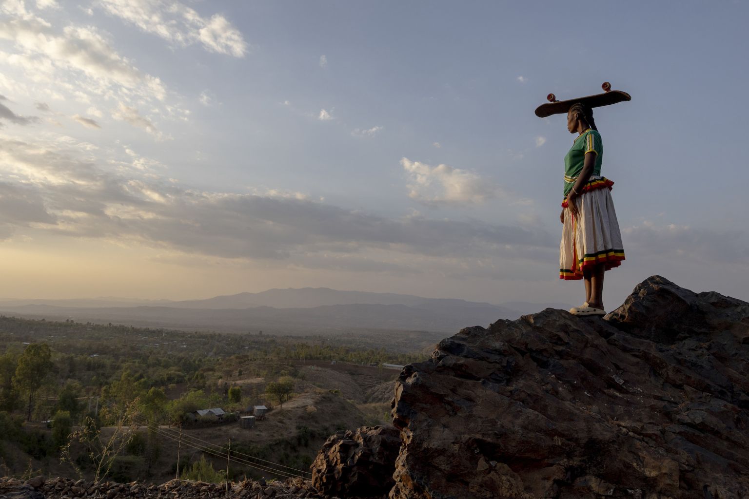 femme sur une colline, avec une planche de skate sur la tête