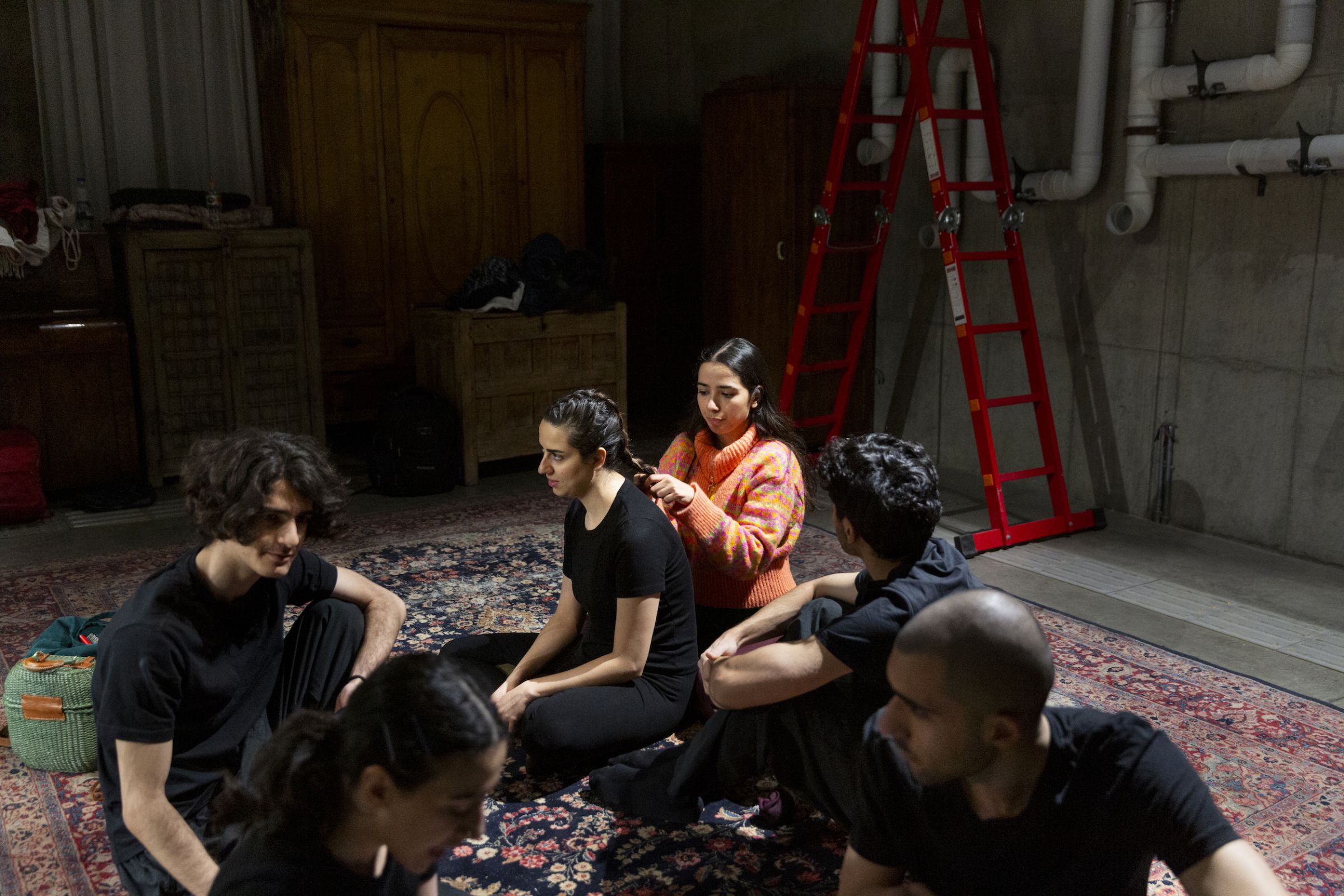 Une troupe de danseur assis sur un tapis, une danseuse se fait coiffer