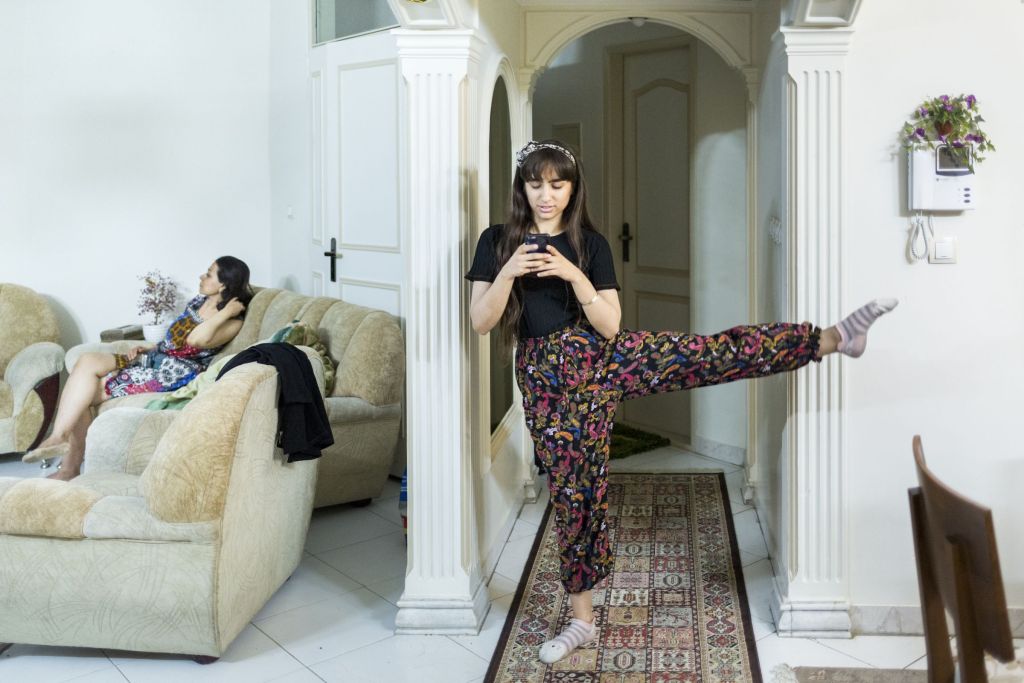 Une jeune femme dans un salon fait des &eacute;tirements, une jambe en l'air en regardant son portable