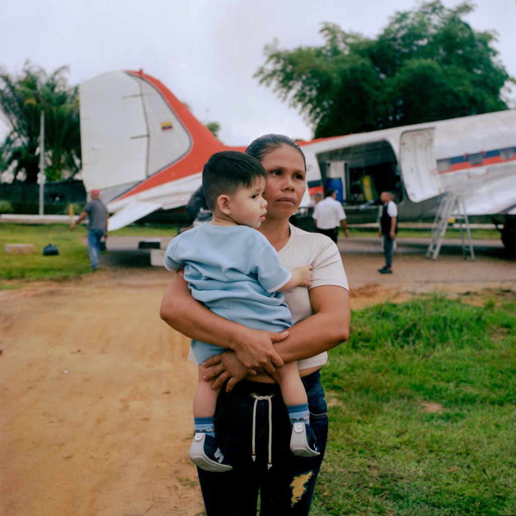 Une Colombienne et son enfant dans les bras devant un avion