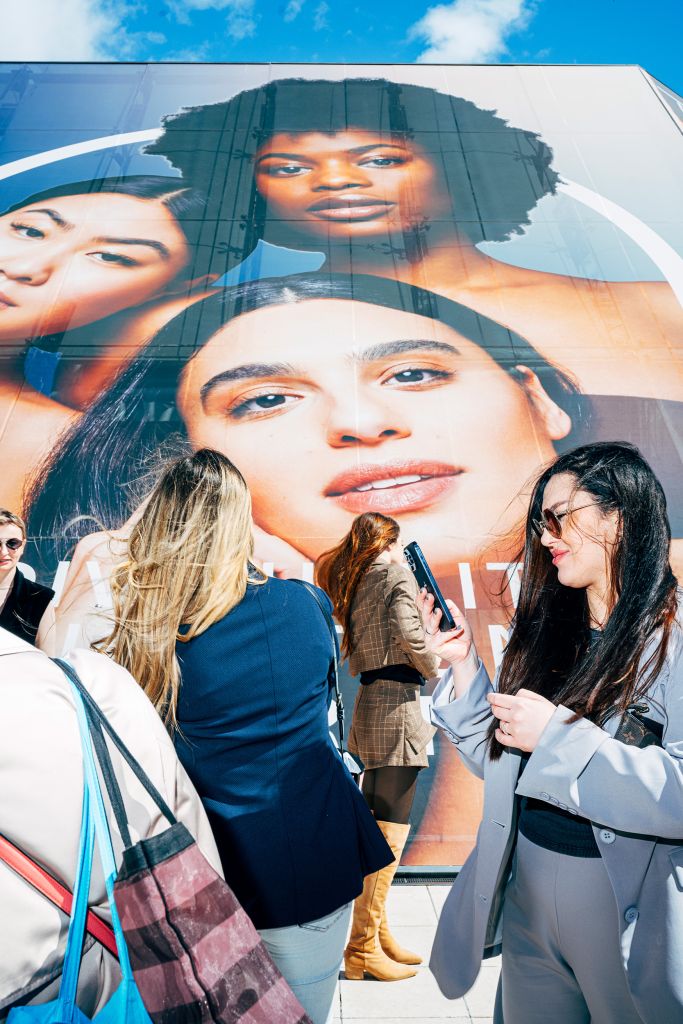 Des femmes devant une grande affiche de visages de femmes