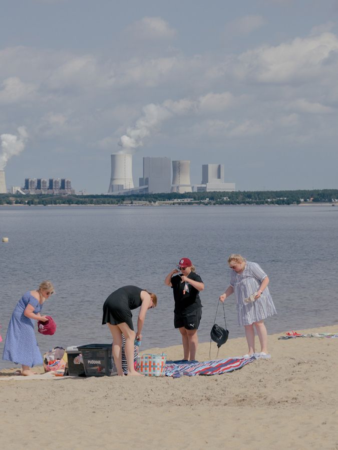 Des femmes sur une plage devant un lac et une centrale à charbon