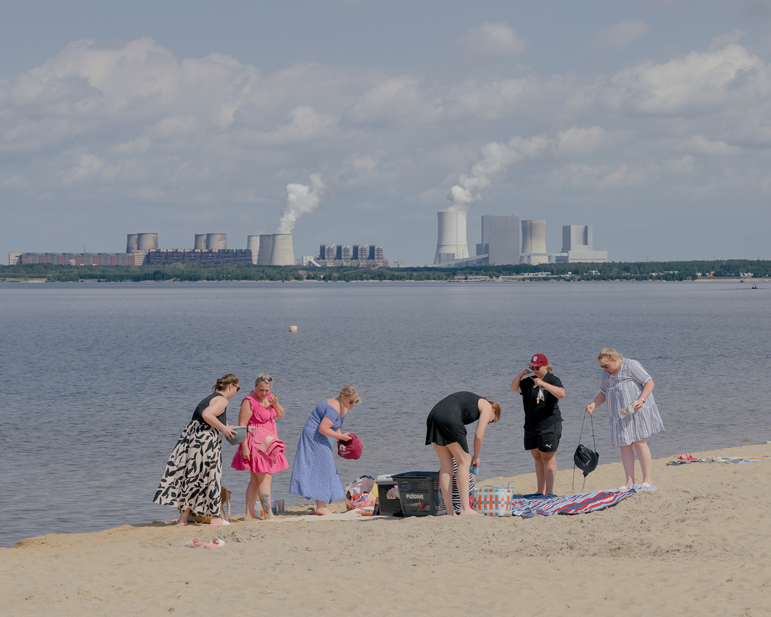 Des femmes sur une plage devant un lac et une centrale à charbon
