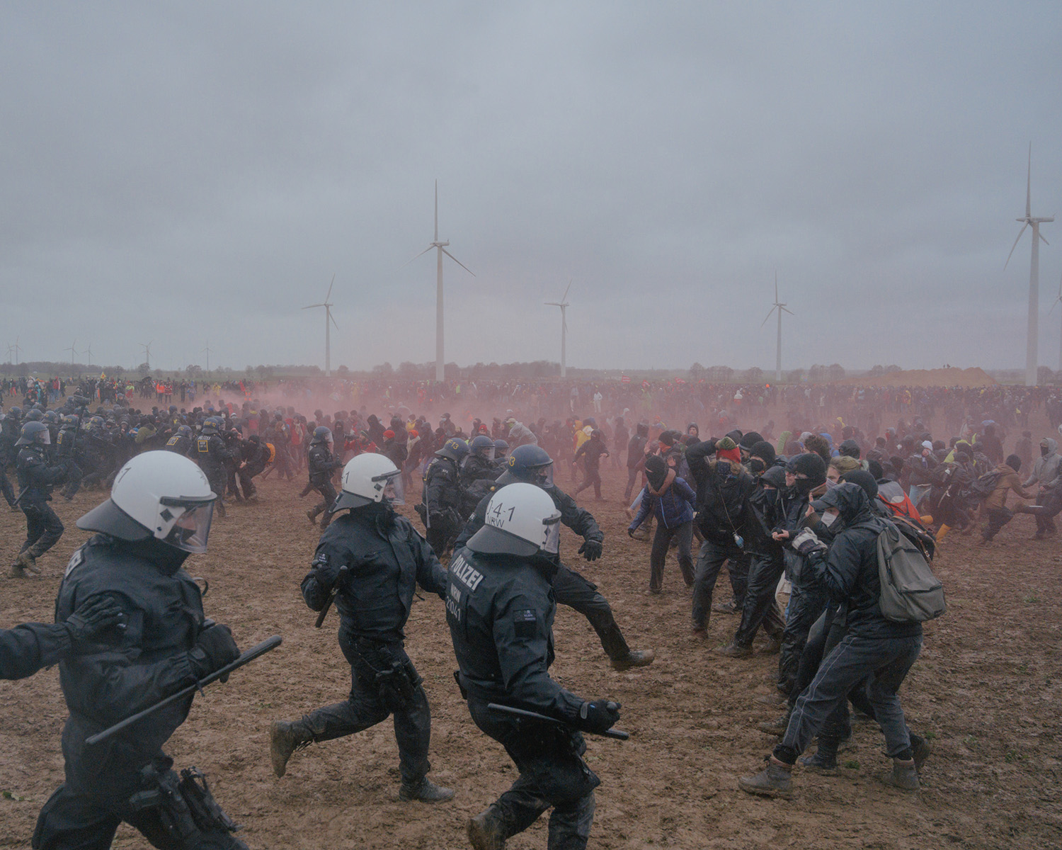 Des policier casqués cous vers des militants écologistes avec des éoliennes en arrière plan